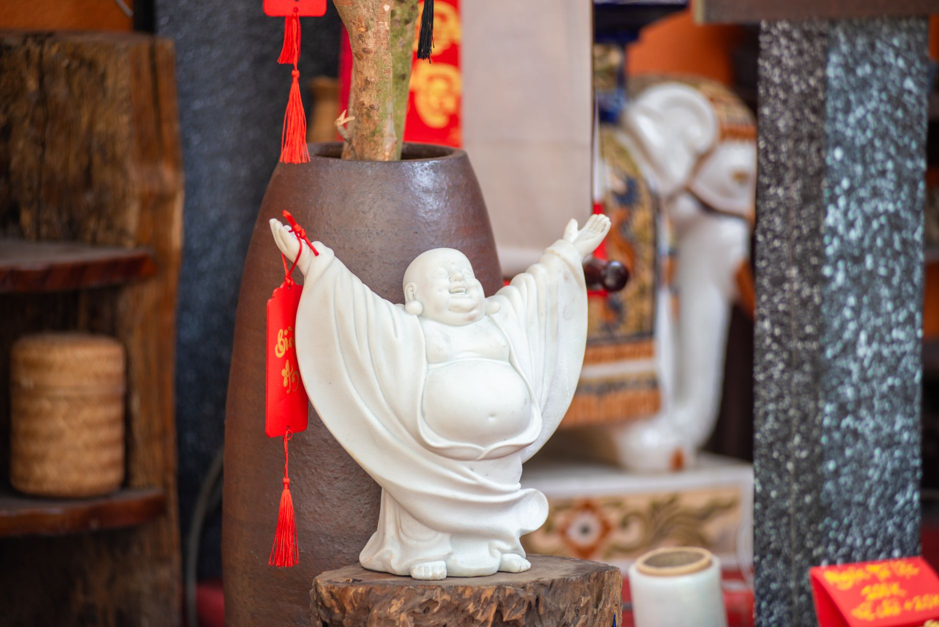 White Laughing Buddha statue with red tassel decoration in vibrant Asian interior.