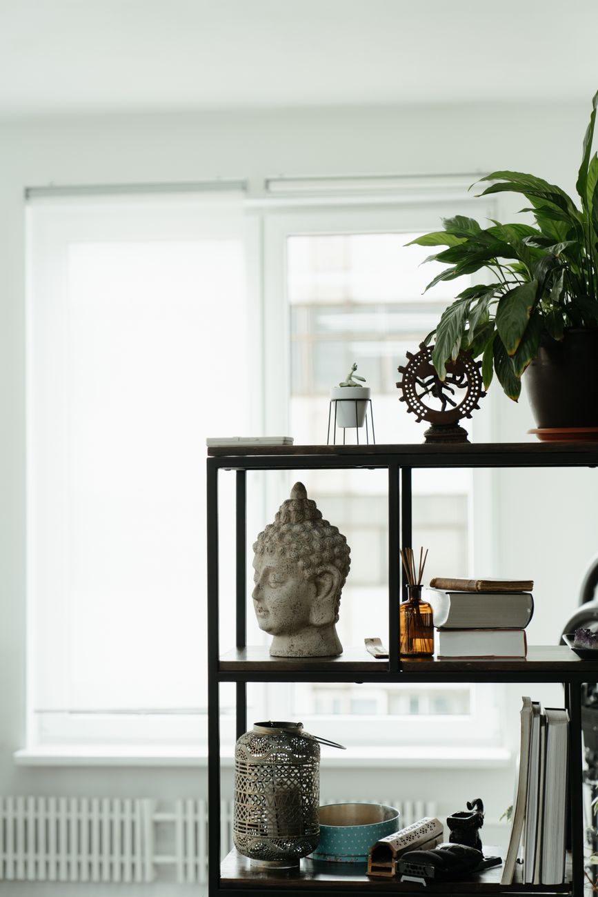 Shelf with Buddha sculpture, books, and a plant in a serene indoor setting.